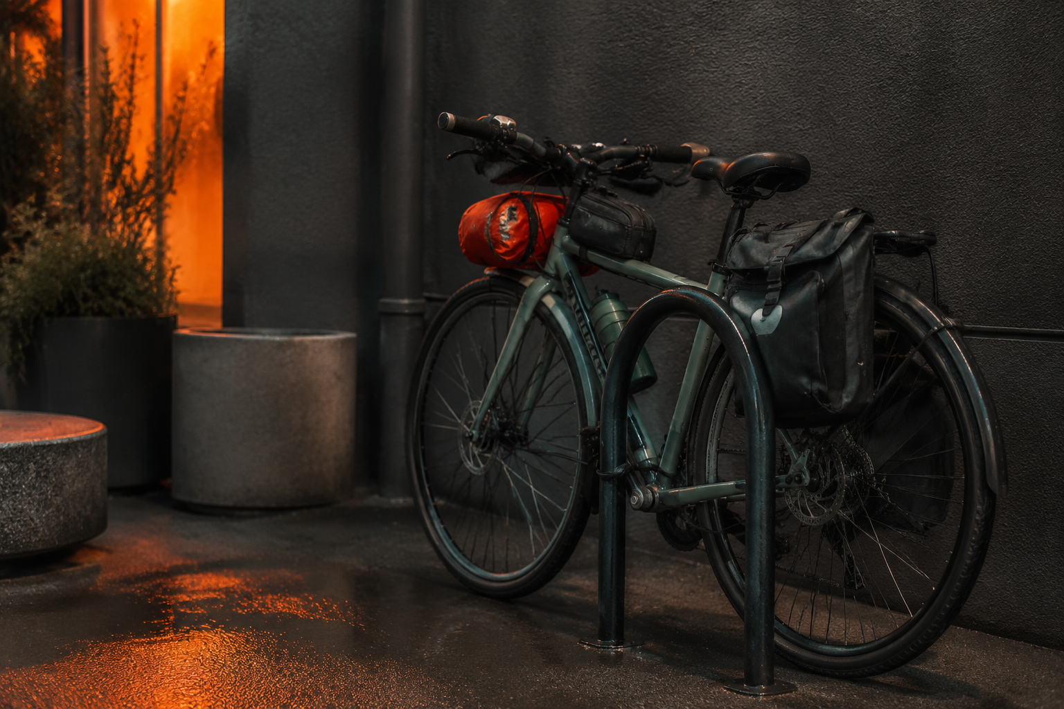 A quiet city bike-parking corner at dusk with commuter bags mounted on a locked bicycle